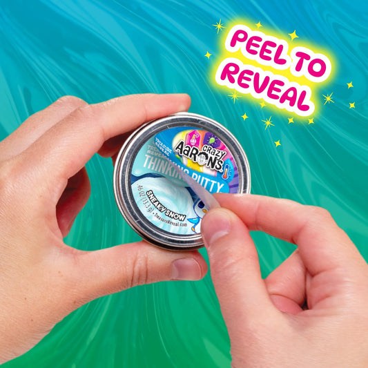 Hands peeling the mystery label from a Crazy Aaron's Treasure Reveal Thinking Putty tin.