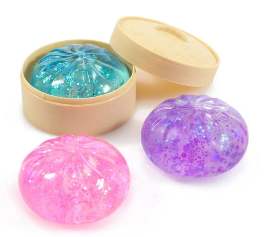 Pink, purple, and blue glitter Squish N' Sparkle dumplin' squishies with a tan steamer-style case