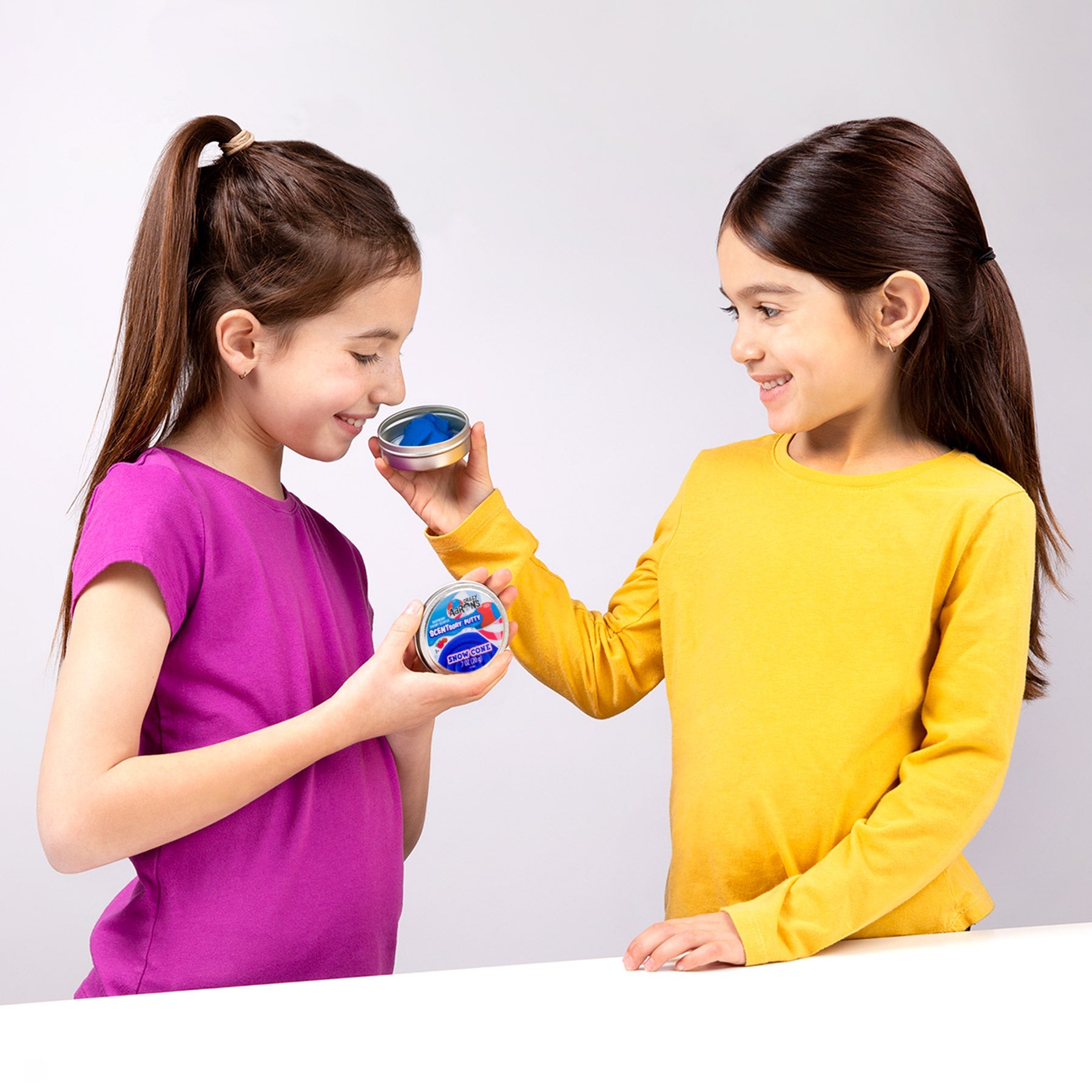 Child smelling Snow Cone SCENTsory Thinking Putty while another child holds the collectible tin.