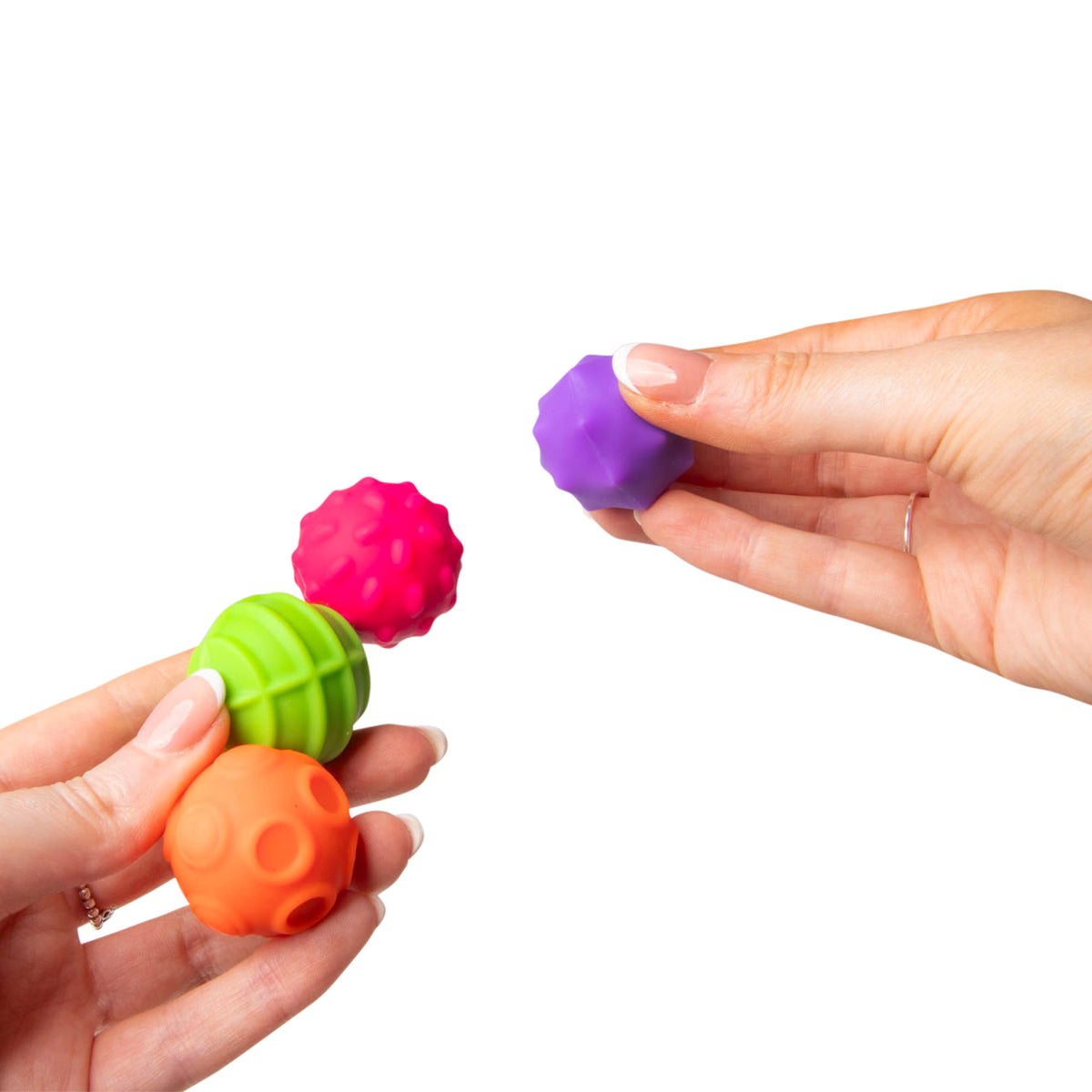 Two hands passing a purple faceted magnetic sensory sphere with the other three balls held nearby