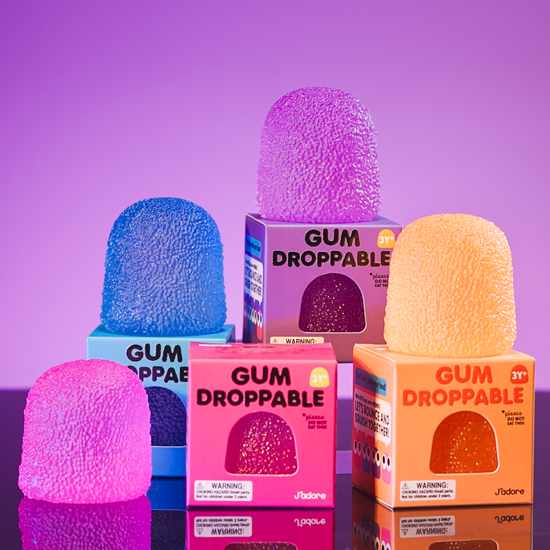 J'adore Gum Droppable boxes and squishies in blue, purple, pink, and orange on a purple background