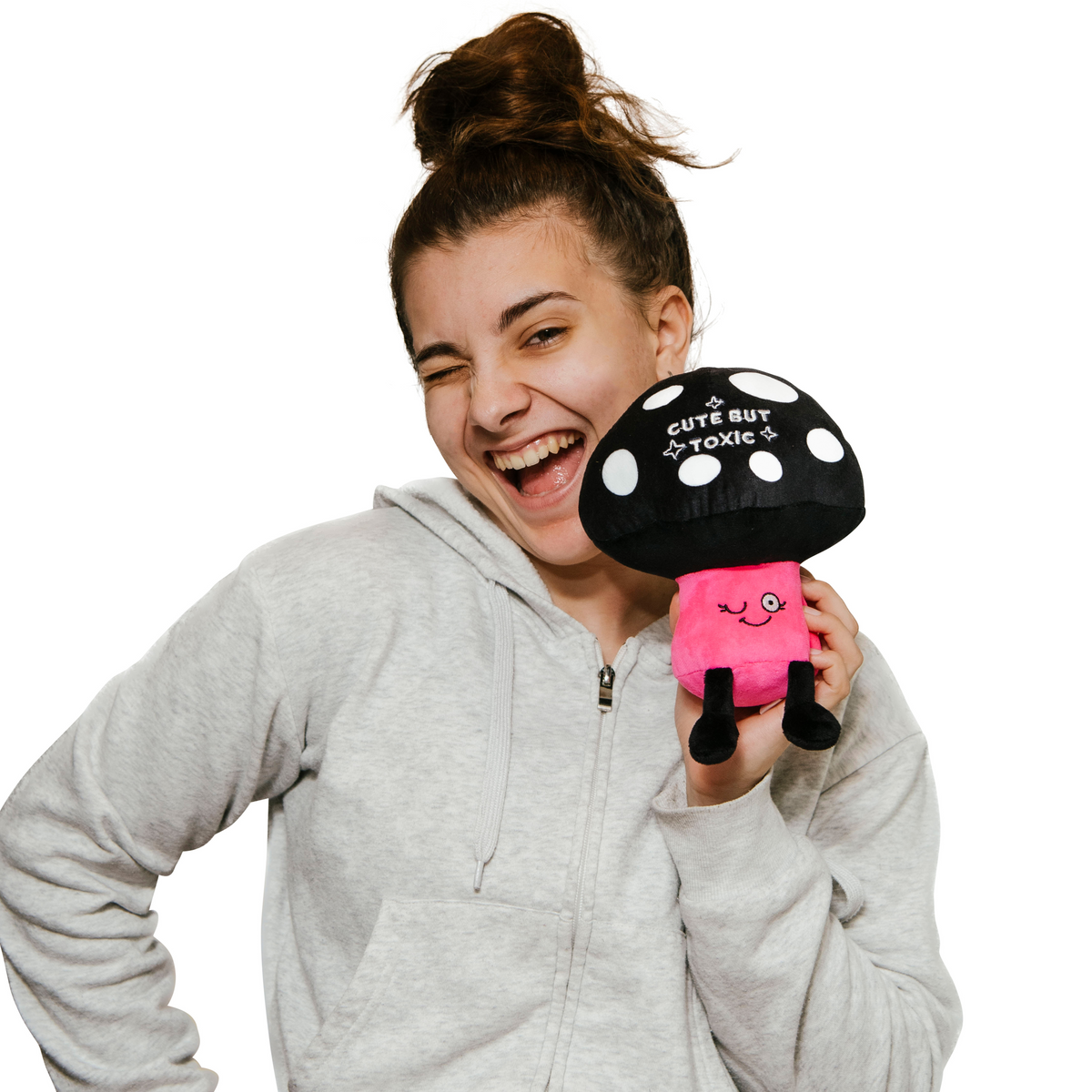Laughing woman winking while holding the Cute but Toxic mushroom plush to show its size