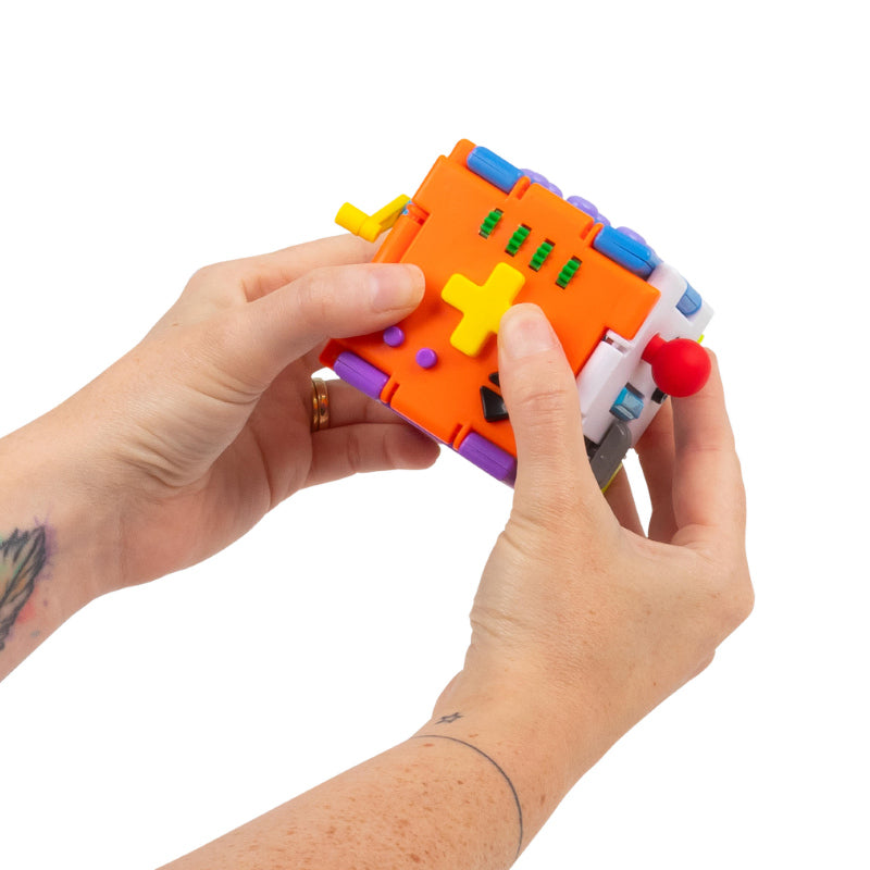 Hands pressing the cross-shaped button on the Super Sensory Square fidget cube