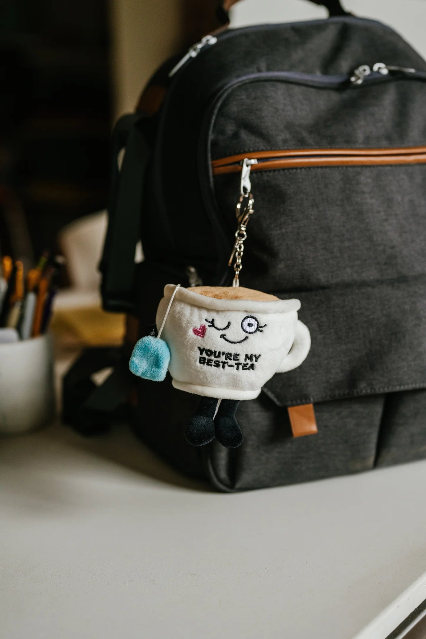 Cute plush teacup bag charm attached to a black handbag
